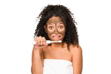 Young african american woman toothbrushing and applying herself a facial mask isolated