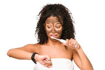 Young african american woman preparing to go out for dinner brushing her teeth looking at the time on the clock