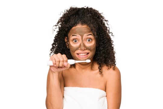 Young african american woman toothbrushing and applying herself a facial mask isolated