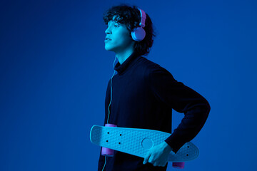 Male teenager in headphones listening to music with skateboard in hand, hipster lifestyle, portrait...