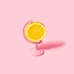 Monochromatic fruit concept. Orange slice as globe on pastel light pink background. Minimalistic juicy food composition. Creative summer nature idea.