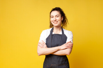 portrait of young barista girl in uniform on a yellow background, a woman waiter stands with...