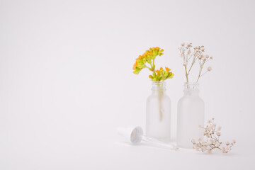 Fototapeta na wymiar Glass skin care bottle mock up with yellow flower and white flower on white background with the copy space. The beauty background, Art, and design. 