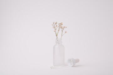 skincare glass bottle with dropper and flower on white background with copy space.