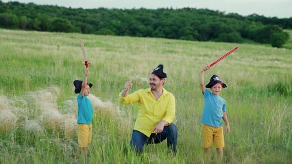 Happy dad kids play pirates together on green grass. Pirate father, child with saber, family games...