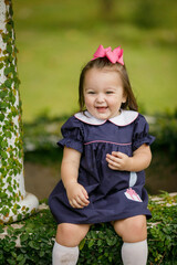 A cute little two year old toddler girl sitting outside in a navy blue dress