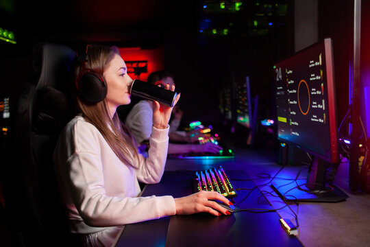 girl gamer sits at a computer and drinks an energy drink, a woman plays in a computer club at night and holds a drink