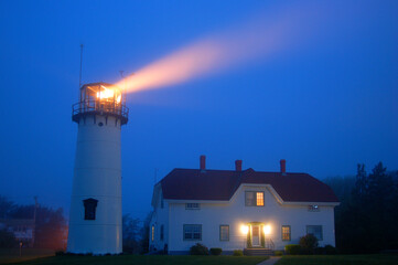 A beacon from the Chatham lighthouse on Cape Cod shines through the foggy and misty sky © kirkikis