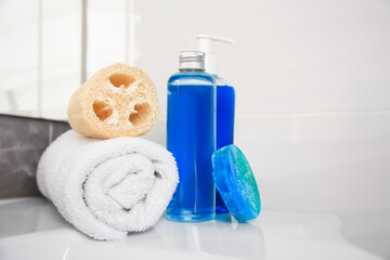 Loofah sponge, rolled towel and cosmetic products on sink in bathroom