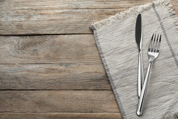 Fork, knife and napkin on wooden table, top view with space for text. Stylish shiny cutlery set - obrazy, fototapety, plakaty