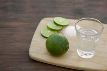 Mexican tequila shot with lime slices on wooden table, closeup and space for text. Drink made from agave