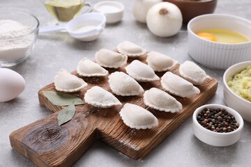 Raw dumplings (varenyky) and ingredients on grey table