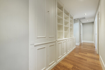 Distributor corridor of a house with reddish wooden floors, bookcase with white lacquered wooden shelves