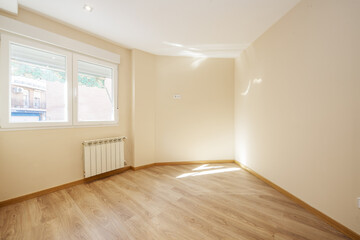 Empty living room with oak laminate flooring, cream painted walls and aluminum window over a white radiator