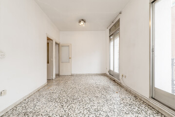 Empty living room with white terrazzo floor with black dots, white walls, wooden access doors and...