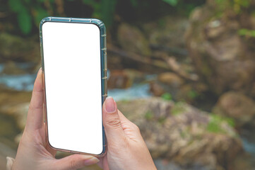 Women using a smartphone with empty white screen at the outdoor with forest at the background.