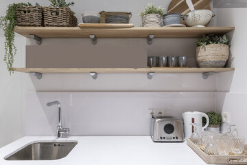 Kitchen with white worktop with stainless steel sink and ecru wooden shelves with kitchen accessories