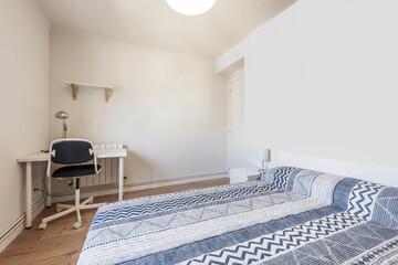 A bedroom with a double bed with a blue patterned bedspread, a white desk with a swivel chair with chestnut hardwood floors and a white wooden front door