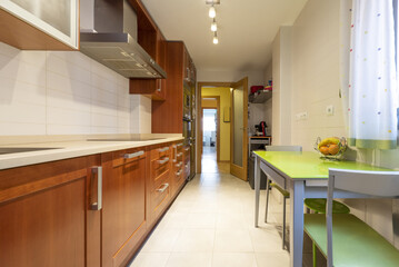 apartment kitchen with redwood cabinets with white stone countertop, kitchen table with green tempered glass top and matching chairs