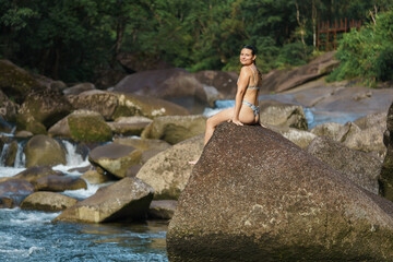 Fototapeta na wymiar Young and sexy woman stand on rock wearing swimsuit on the beautiful river in the jungle