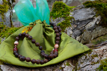 A close up image of wooden prayer beads and a green silk pouch resting on a moss covered tree...