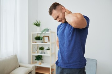 Man back neck and shoulder pain, inflammation of muscles and ligaments rupture during sports, inflammation and injury, in a blue t-shirt at home