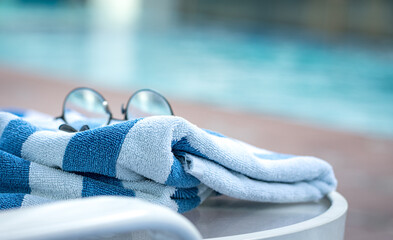 Pool towel on lounge chair with eyeglasses and pool background. Summer vacation concept.
