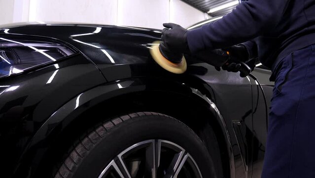 A man polishes a black car with a polishing machine in a car dealership. Car care in an auto repair shop.
