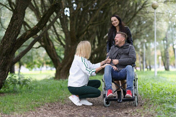 Friends kidding and laughing while walking in park, one male friend sitting in wheelchair.
