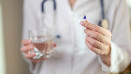 Doctor holds pill in one hand and glass of water in other.