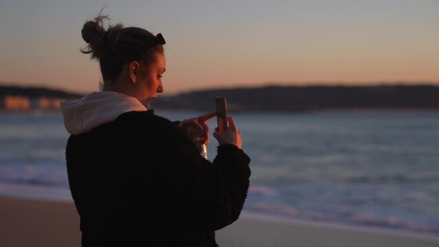 Young beautiful woman on vacation taking pictures with her smartphone during sunset
