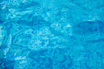 Top view of the water in a deep blue pool lined with small square tiles. Clear blue water in a pool with shallow waves
