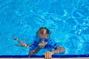 Child clamps his nose with his hand and holds his breath, dives in a pool of warm water. Boy swims underwater in the outdoor pool