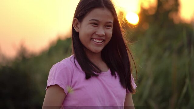 Portrait of a cute little girl smiles looking at camera in sunset
