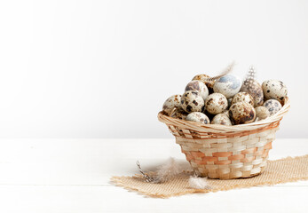 Small woven basket full of organic farmer quail eggs on burlap napkin on white. Easter. Copy space.