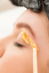 Young woman undergoing eyebrow correction procedure in beauty salon, closeup. Dying eyebrows whith brush