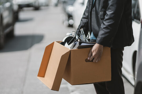 Businessman Fired Or Resign From The Company Are Carrying Boxes Down The Street Looking For A New Job. Unemployed, Hiring Job, Quitting Job Concept..