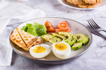 Sliced avocado, soft boiled egg, tomatoes and toast on a plate. Homemade breakfast.