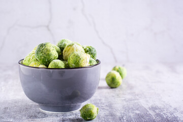 Frozen Brussels sprouts in a bowl on a gray background. Vegetarian food.