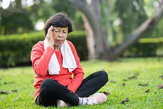Senior asian woman hand holding head pain have a headache after running in park. Old asian woman resting at the park garden and holding painful headache or heat stroke symptoms. Sport health concept.