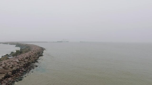 Aerial view of big ferry ship Stena Line arriving at Port of Liepaja (Latvia), passenger and vehicle transportation, dull foggy day with heavy mist, distant establishing drone shot moving forward