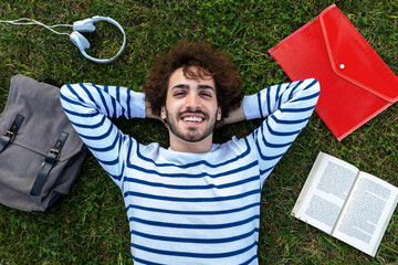Top view of happy, smiling young caucasian man relaxing lying down on grass looking at camera.