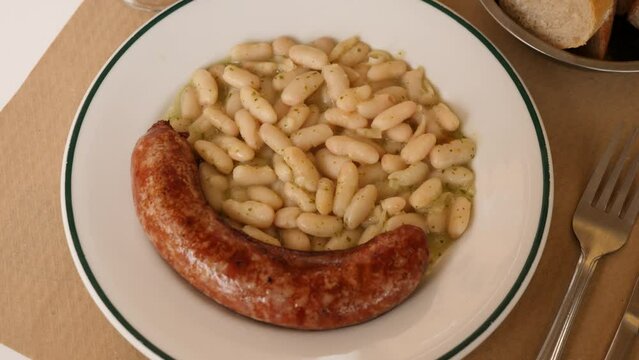 Botifarra amb mongetes, representative dish of Catalan home cooking - traditional fried botifarra sausage served with cooked white beans