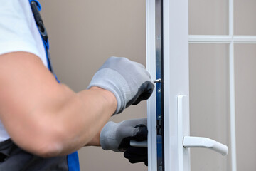 Close-up professional craftsman in gloves repairs the lock on the white plastic door. Professional...