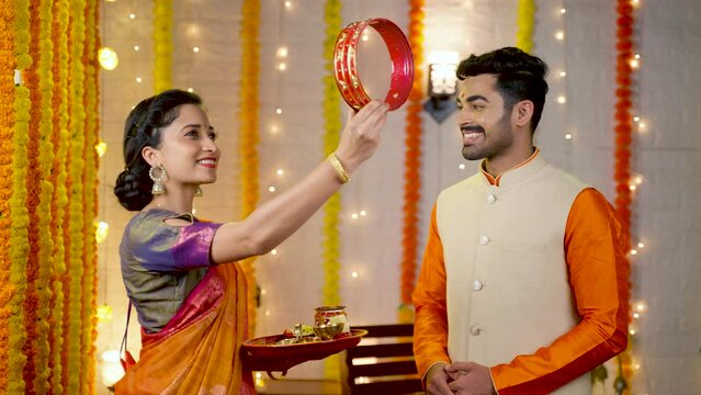 Wife looking husband face through sieve during karva Chauth festival celebration - concept of Indian custom, tradition and belief