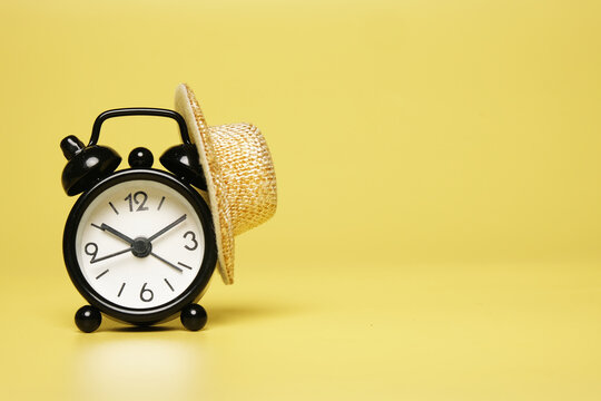 A picture of alarm clock with straw hat on copyspace yellow background. Flexible time working hours concept.