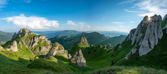 Panorama of green meadow with rocks and rocky mountains in romanian mountains in muntii ciucas with setting sun