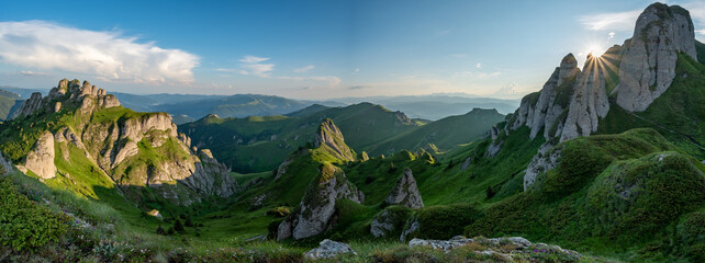 Panorama of green meadow with rocks and rocky mountains in romanian mountains in muntii ciucas with setting sun