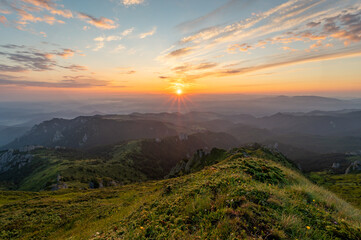 Obraz premium Green meadow with rocks and rocky mountains in romanian mountains in muntii ciucas with raising sun