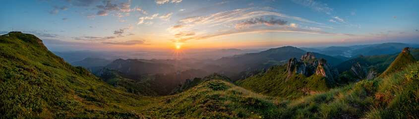 Panorama of green meadow with rocks and rocky mountains in romanian mountains in muntii ciucas with raising sun